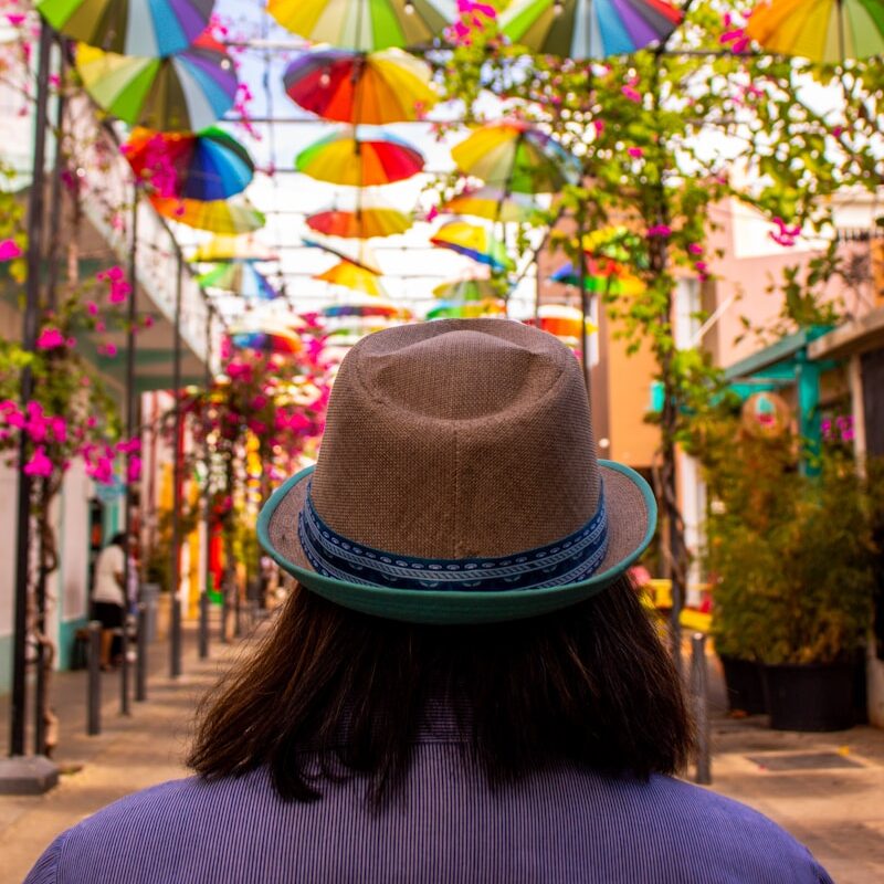 a man with a hat is looking up at colorful umbrellas